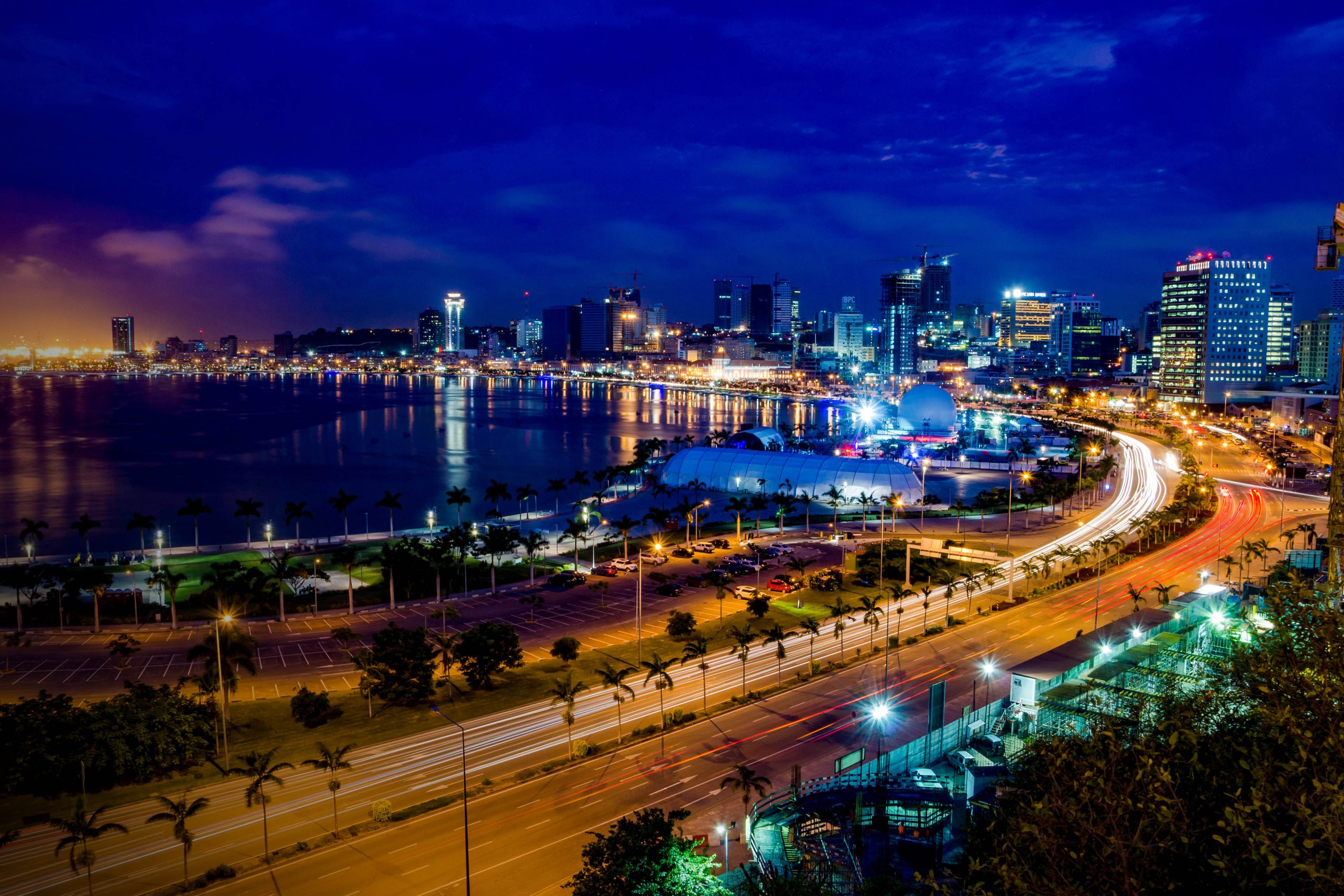 Skyline of Luanda and its seaside during the blue hour. Many lights and high rise buildings.